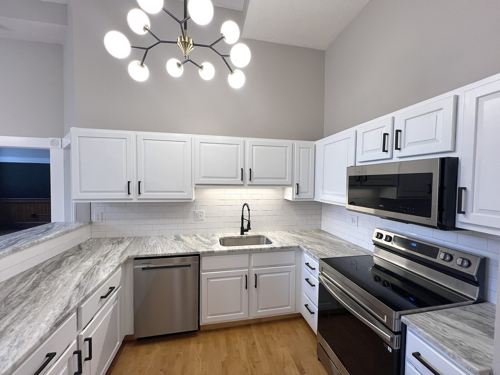 White kitchen with vaulted ceiling, statement chandelier, and quartzite countertops
