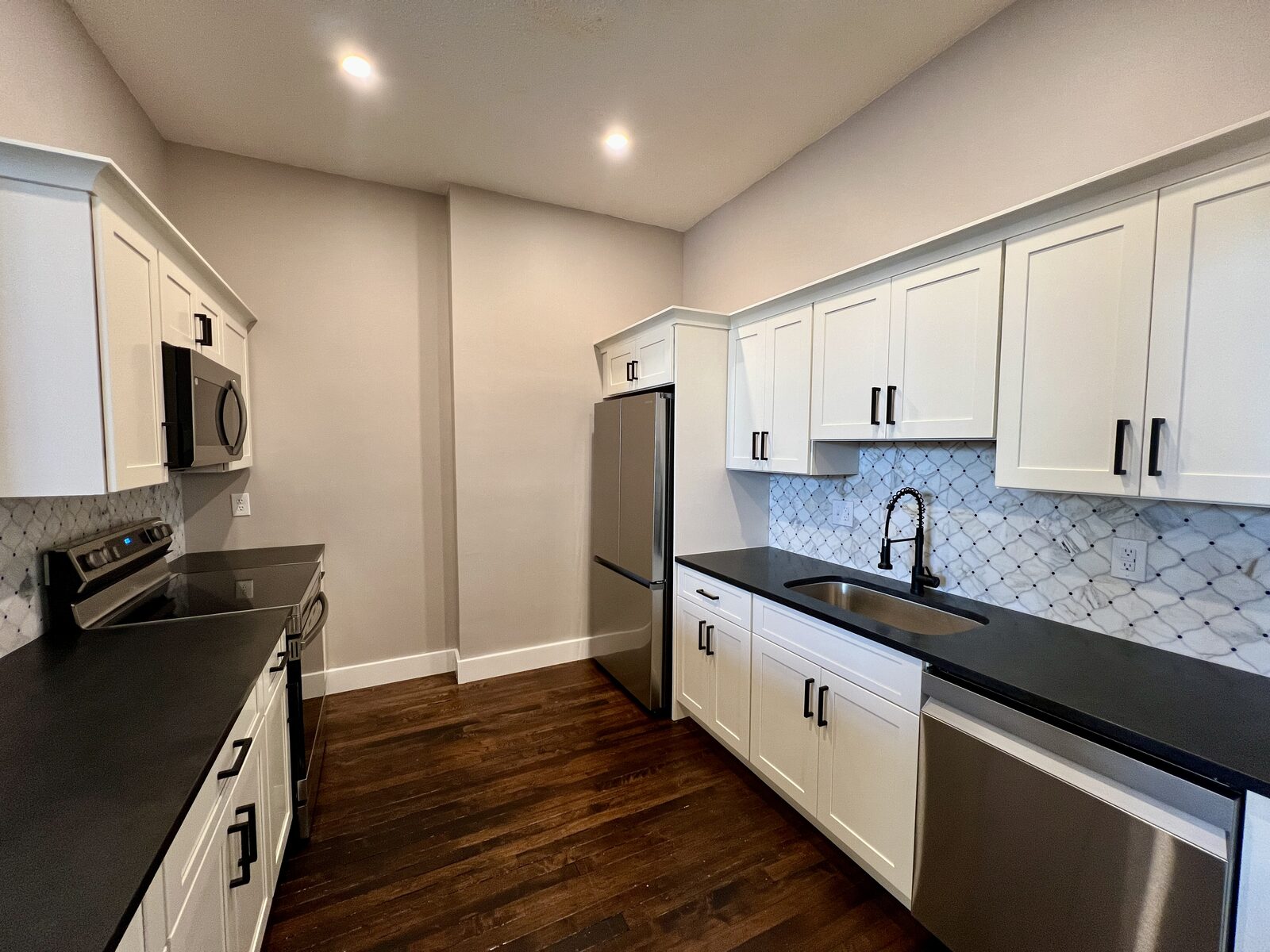 Galley kitchen with white cabinetry, black countertops, and mosaic tile backsplash